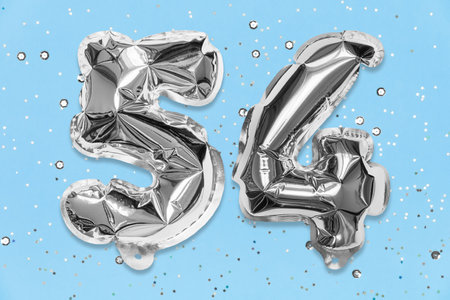Silver foil balloon number, digit fifty four on a blue background with sequins. Birthday greeting card with inscription 54. Top view. Numerical digit. Celebration event, template.の写真素材