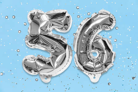 Silver foil balloon number, digit fifty six on a blue background with sequins. Birthday greeting card with inscription 56. Top view. Numerical digit. Celebration event, template.の写真素材