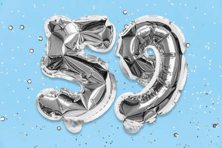 Silver foil balloon number, digit fifty nine on a blue background with sequins. Birthday greeting card with inscription 59. Top view. Numerical digit. Celebration event, template.の写真素材
