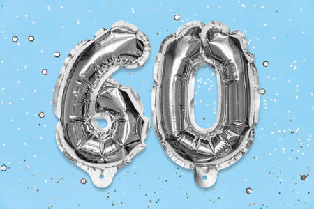 Silver foil balloon number, digit sixty on a blue background with sequins. Birthday greeting card with inscription 60. Anniversary concept. top view. Numerical digit. Celebration event template.の写真素材