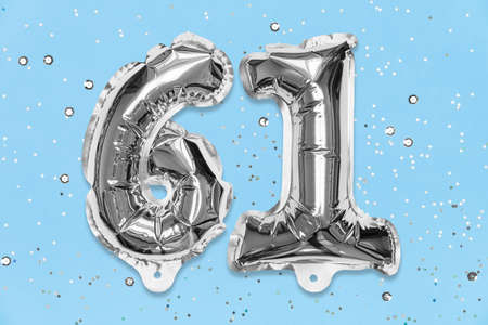 Silver foil balloon number, digit sixty one on a blue background with sequins. Birthday greeting card with inscription 61. Top view. Numerical digit. Celebration event, template.の写真素材