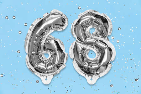 Silver foil balloon number, digit sixty eight on a blue background with sequins. Birthday greeting card with inscription 68. Top view. Numerical digit. Celebration event, template.の写真素材