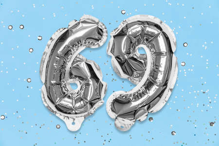 Silver foil balloon number, digit sixty nine on a blue background with sequins. Birthday greeting card with inscription 69. Top view. Numerical digit. Celebration event, template.の写真素材
