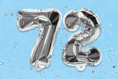 Silver foil balloon number, digit seventy two on a blue background with sequins. Birthday greeting card with inscription 72. Top view. Numerical digit. Celebration event, template.の写真素材