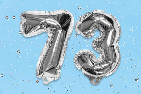 Silver foil balloon number, digit seventy three on a blue background with sequins. Birthday greeting card with inscription 73. Top view. Numerical digit. Celebration event, template.の写真素材
