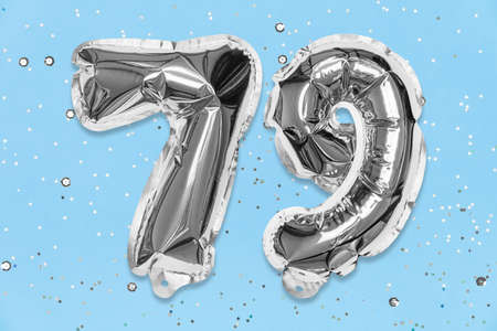 Silver foil balloon number, digit seventy nine on a blue background with sequins. Birthday greeting card with inscription 79. Top view. Numerical digit. Celebration event, template.の写真素材