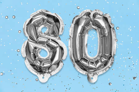 Silver foil balloon number, digit eighty on a blue background with sequins. Birthday greeting card with inscription 80. Anniversary concept. top view. Numerical digit. Celebration event template.の写真素材