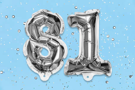 Silver foil balloon number, digit eighty one on a blue background with sequins. Birthday greeting card with inscription 81. Top view. Numerical digit. Celebration event, template.の写真素材