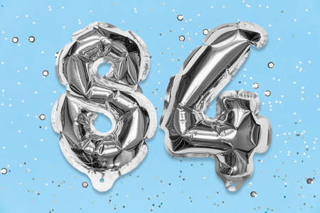 Silver foil balloon number, digit eighty four on a blue background with sequins. Birthday greeting card with inscription 84. Top view. Numerical digit. Celebration event, template.の写真素材