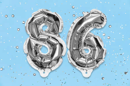 Silver foil balloon number, digit eighty six on a blue background with sequins. Birthday greeting card with inscription 86. Top view. Numerical digit. Celebration event, template.の写真素材