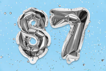 Silver foil balloon number, digit eighty seven on a blue background with sequins. Birthday greeting card with inscription 87. Top view. Numerical digit. Celebration event, template.の写真素材