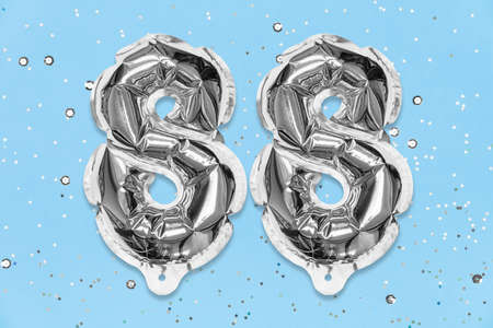Silver foil balloon number, digit eighty eight on a blue background with sequins. Birthday greeting card with inscription 88. Top view. Numerical digit. Celebration event, template.の写真素材