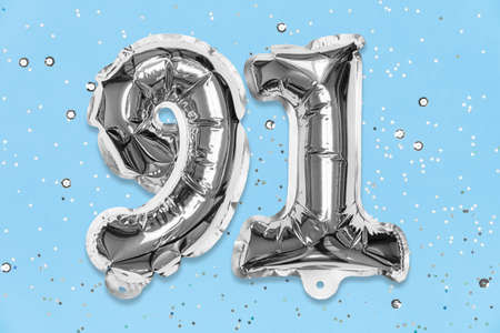 Silver foil balloon number, digit ninety one on a blue background with sequins. Birthday greeting card with inscription 91. Top view. Numerical digit. Celebration event, template.の写真素材