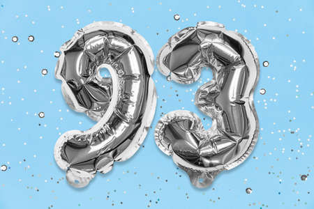 Silver foil balloon number, digit ninety three on a blue background with sequins. Birthday greeting card with inscription 93. Top view. Numerical digit. Celebration event, template.の写真素材