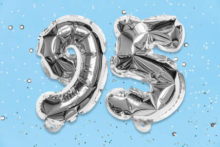 Silver foil balloon number, digit ninety five on a blue background with sequins. Birthday greeting card with inscription 95. Anniversary concept. Numerical digit. Celebration event template.の写真素材