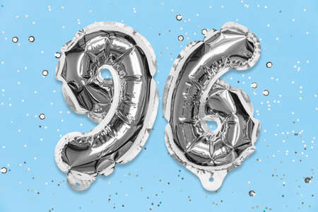 Silver foil balloon number, digit ninety six on a blue background with sequins. Birthday greeting card with inscription 96. Top view. Numerical digit. Celebration event, template.の写真素材