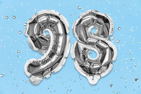 Silver foil balloon number, digit ninety eight on a blue background with sequins. Birthday greeting card with inscription 98. Top view. Numerical digit. Celebration event, template.の写真素材