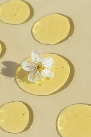 Drops of transparent cosmetic gel or serum yellow with a white flower on a beige background. The concept of natural cosmetics. top view. selective focusの写真素材