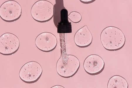 Drops of serum or hyaluronic acid gel with a pipette on a pink background. Smears of cosmetic skin care products. wellness and beauty conceptの写真素材