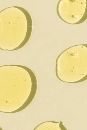 Drops of transparent cosmetic gel or serum yellow on a beige background. The concept of cosmetics or virus protection. top viewの写真素材