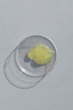 A smear, a drop of scrub, gel or fluid in a Petri dish on a gray background. Concept of cosmetics laboratory researches. Smear of skincare cosmetics product. wellness and beauty conceptの写真素材