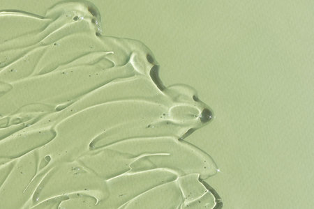 Transparent serum gel with hyaluronic acid for the face on a green background. The texture of a...