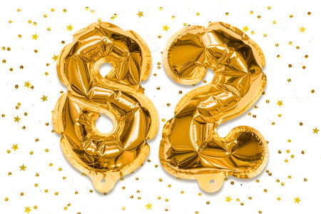The number of the balloon made of golden foil, the number eighty-two on a white background with sequins. Birthday greeting card with inscription 82. Numerical digit, Celebration event.の写真素材