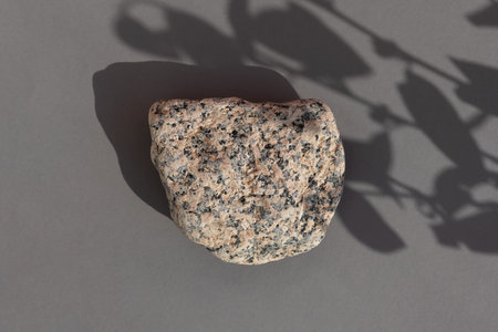 Abstract empty podium made of multicolored stone on a gray background with leaves shadows. Showcase...