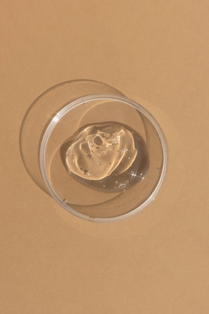 Hyaluronic acid serum or gel for the face in Petri dish on a beige background. Concept of cosmetics laboratory researches, wellness and beauty. cosmetic texture. top viewの写真素材