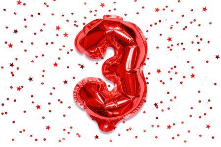 The number of the balloon made of red foil, the number three on a white background with sequins. Birthday greeting card with inscription 3. Numerical digit, Celebration event.の写真素材