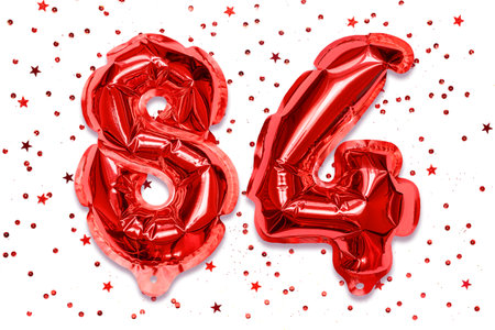 The number of the balloon made of red foil, the number eighty-four on a white background with sequins. Birthday greeting card with inscription 84. Numerical digit. celebration event.の写真素材