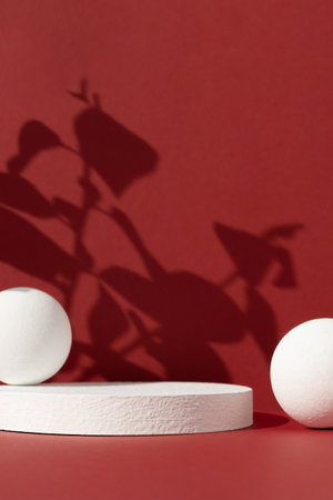 Geometric white podium with balls on an abstract red background with the shadow of plant leaves. Empty scene for the product presentation. Show case, display case.の写真素材