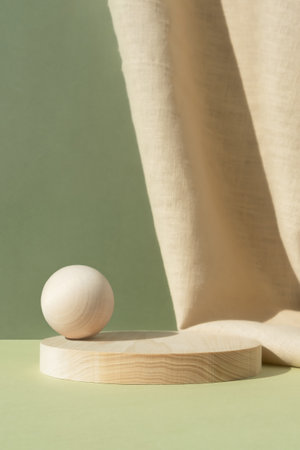 Wooden cylindrical podium, pedestal with ball on a green background with beige curtain. Scene for the presentation of a cosmetic product. empty showcaseの写真素材