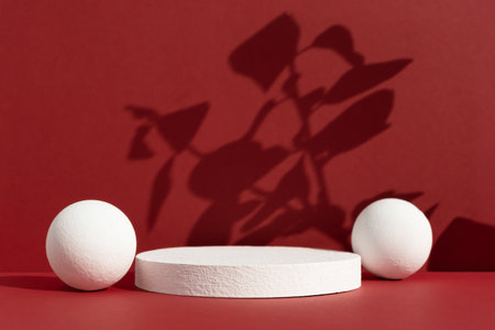 Geometric white podium with balls on an abstract red background with the shadow of plant leaves. Empty scene for the product presentation. Showcase, display case.の写真素材