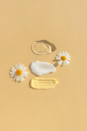 Smears of yellow, white cream and transparent gel or serum with chamomile flowers on a beige background. The texture of a cosmetic skin care product. The concept of natural cosmetics. Top view.の写真素材