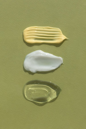 Smears of yellow, white cream and transparent gel or serum on a green background. The texture of a cosmetic skin care product. Top view.の写真素材