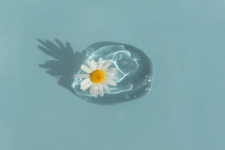 A drop of transparent cosmetic gel or serum with hyaluronic acid with a chamomile flower on a blue background. The concept of natural cosmetics. Cosmetic texture. Top viewの写真素材
