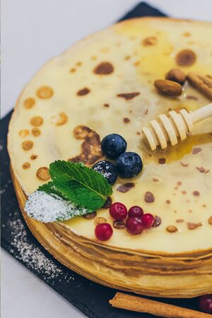 Plate of pancakes dripping with honey with cranberries and blueberries, cinnamon sticks. Shrovetide Maslenitsa Butter Week festival meal. Shrove Tuesday. Pancake day.の写真素材
