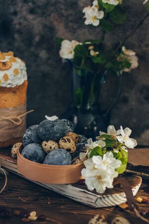 Easter eggs in the round wooden box on rustic wooden background with apple blossom branchの写真素材