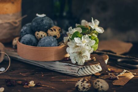 Easter eggs in the round wooden box on rustic wooden background with apple blossom branchの写真素材