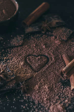 Chocolate bar pieces with cocoa powder and heart shape on dark background, cope space