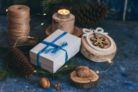 Christmas white gift box with blue bow ribbon, wooden decorations, candle, nuts on magic dark blue...