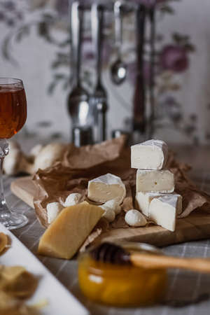 Delicious cheeses on a board with honey and wine on a paper background.の写真素材