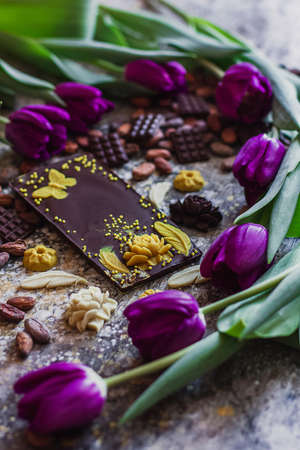 Assortment of different chocolate types in cocoa beans, with violet spring tulips on the background