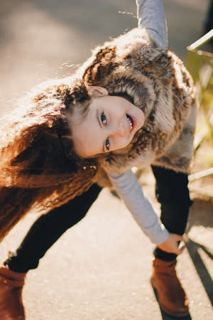 Stylish baby girl 4-5 year old wearing boots, fur coat, moving and playing. Autumn fall seasonの写真素材