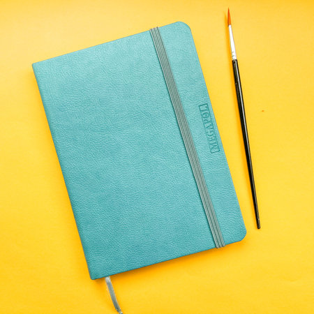 Notepad and diary on a colored background. Colored pencils, compasses, hand draws, children's hand....