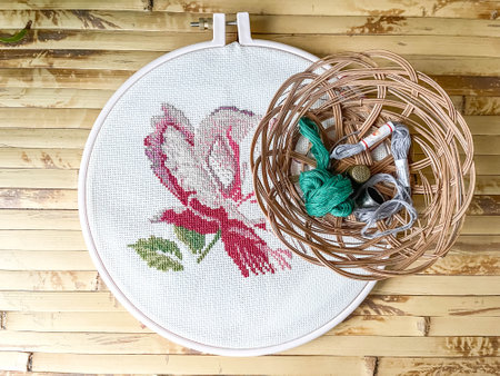 Cross stitch process in the hoop multicolored flower, white canvas, floss threads on bobbins,...