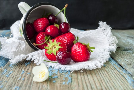 Fresh ripe red strawberries in white enamel mug on wooden background, natural rustic foodの写真素材