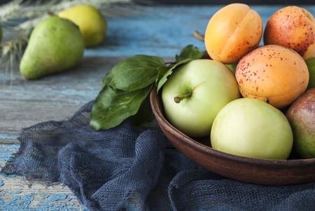 Apples, pears and apricots in a plate on a wooden tableの写真素材