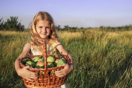 Little girl with blond hair holds a basket of fruitの写真素材